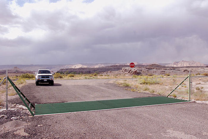 A pick up truck approaching a cattle guard installed in a dirt road.