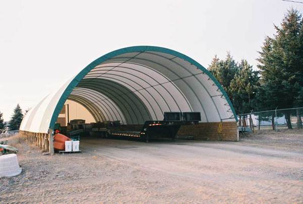 Large curved storage building with vehicles inside, surrounded by trees and a clear sky.